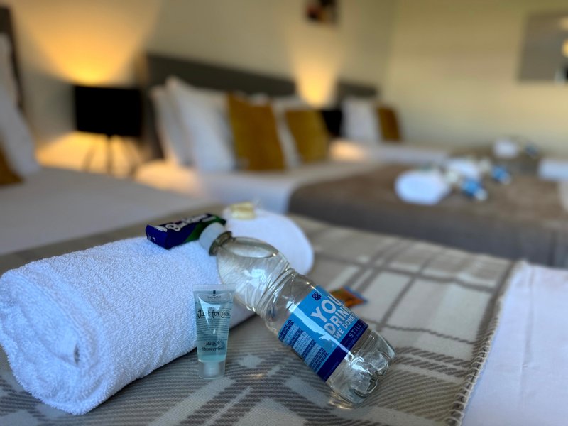 Bedroom with water bottle, rolled towel, and toiletries on bed runner