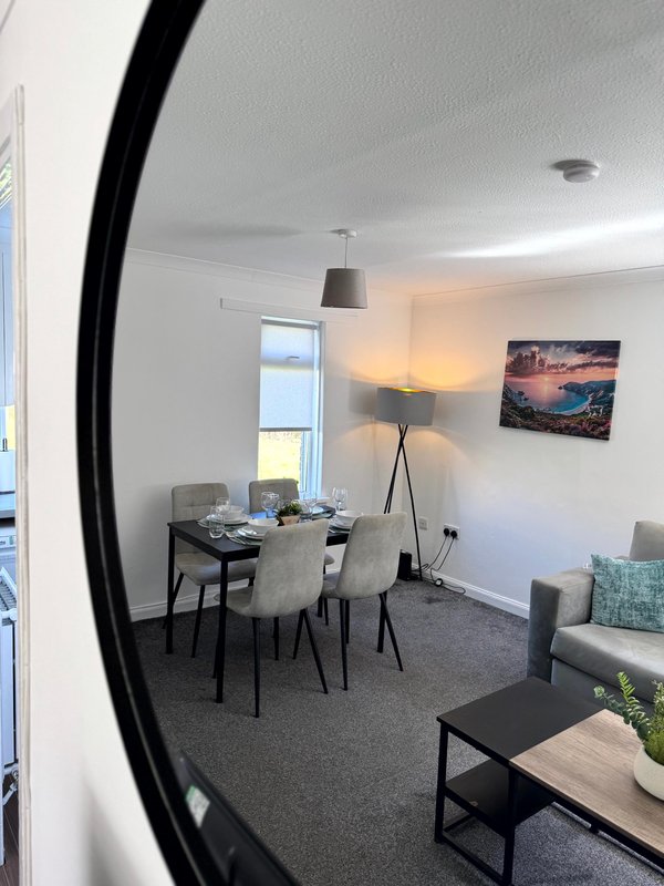 Open-plan living and dining area with desk, round black mirror, pendant light, and framed landscape artwork