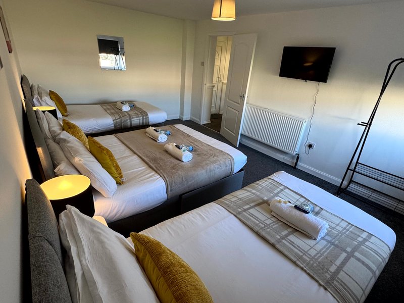 Triple bedroom with three single beds, white bedding, gold cushions and wall-mounted TV