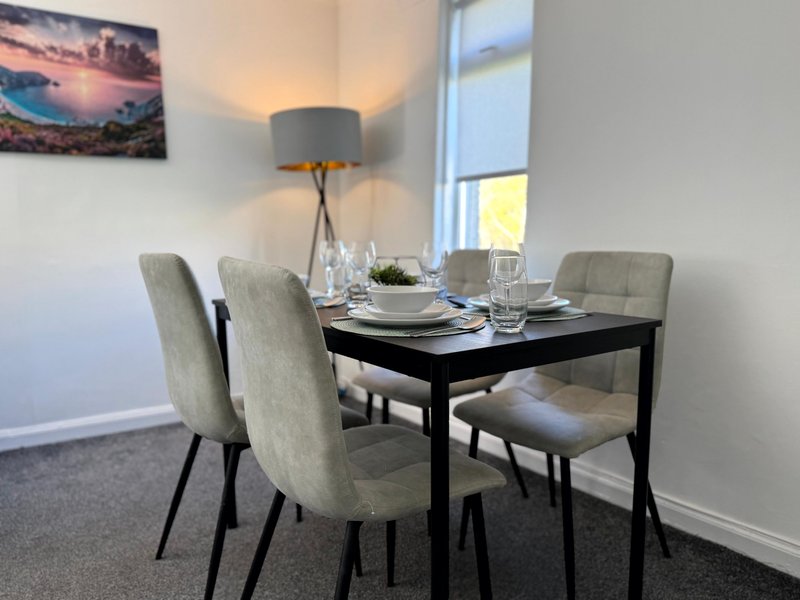 Modern dining room with black table, grey upholstered chairs, pendant lamp and framed landscape artwork