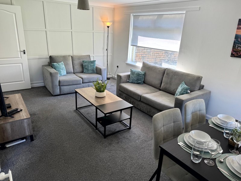 Modern living and dining area with gray sofas, wooden coffee table, place settings and window view