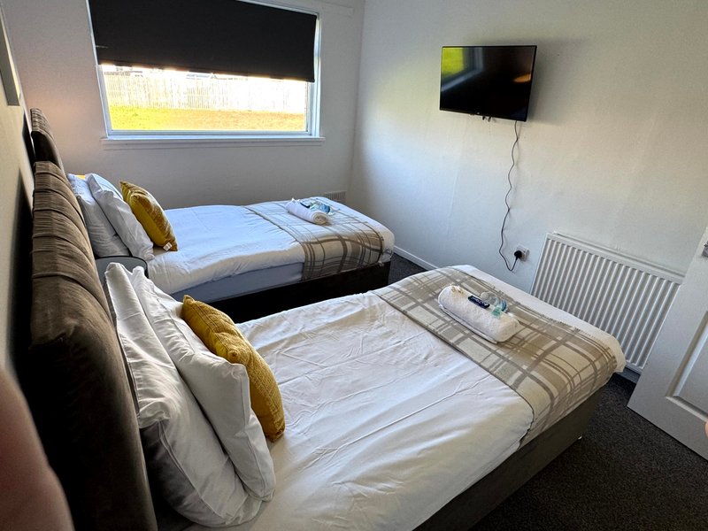 Bedroom with two single beds, gold cushions, wall-mounted TV and window with blind