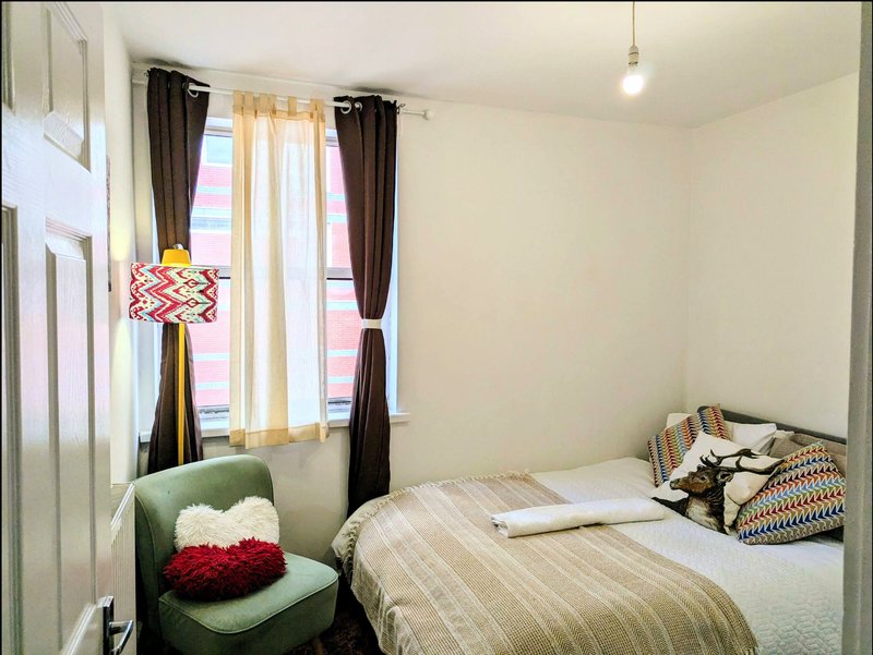 Bedroom with single bed, green chair, window with curtains and pendant lamp