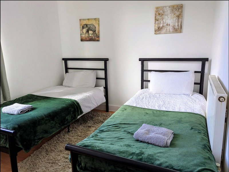 Bedroom with two single beds, green blankets, black frames, and framed wall art