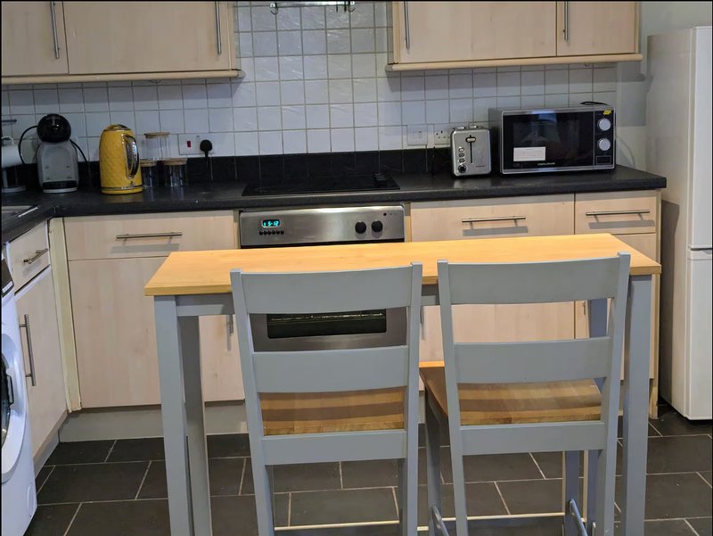 Kitchen with cream cabinets, black countertop, yellow dining table and grey chairs