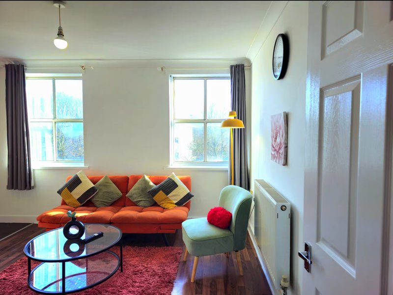Bright living room with orange sofa, colorful cushions, round coffee table and large windows