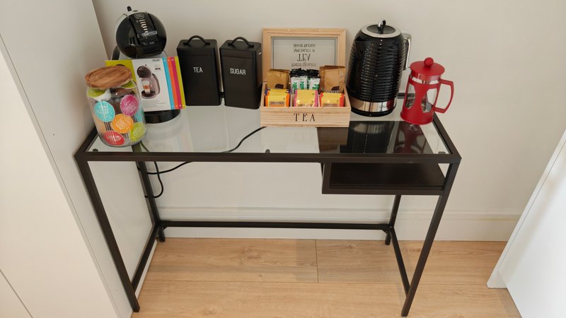 Dark shelving unit with kettle, coffee maker, tea box, and kitchen accessories on wooden floor