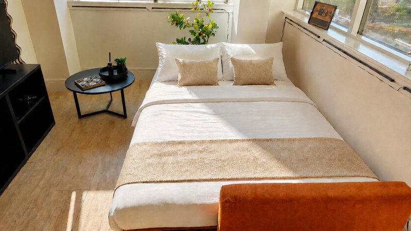Bright bedroom with double bed, cream bedding, cushions, wooden floor and windows