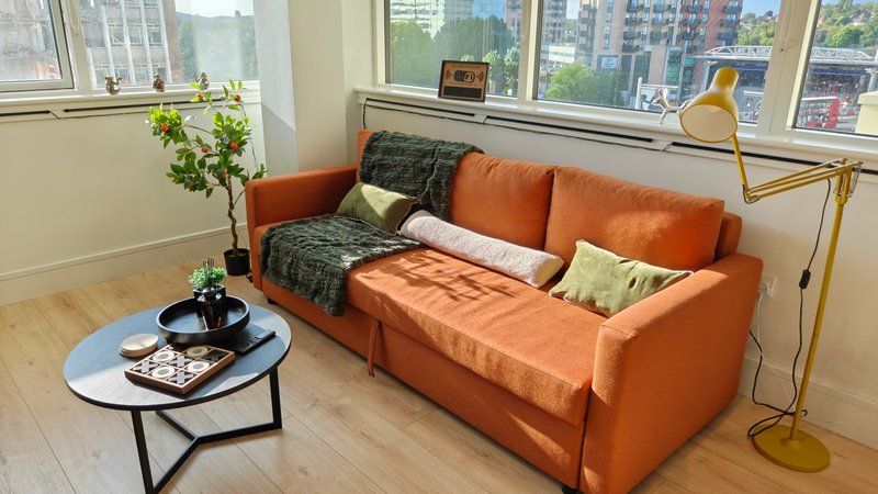 Bright modern living room with orange sofa, coffee table, potted plant and city views