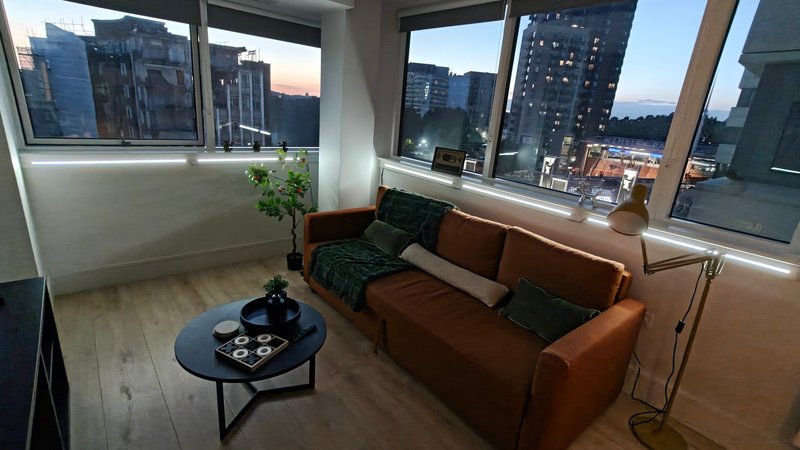 Modern living room with tan leather sofa, black coffee table, and city skyline views through floor-to-ceiling windows