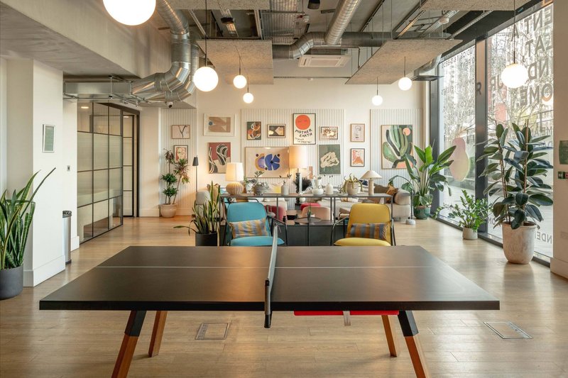 Open-plan office or creative space with ping-pong table, seating area, plants, and framed artwork on walls
