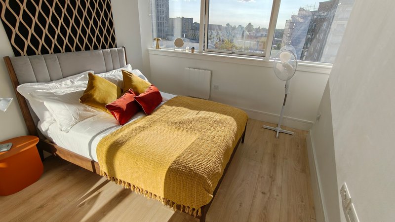 Modern bedroom with double bed, yellow throw, decorative pillows and city skyline view