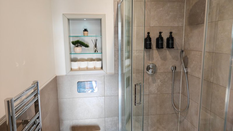 Modern bathroom with walk-in shower, tiled walls, built-in shelf niche with toiletries and towel rack
