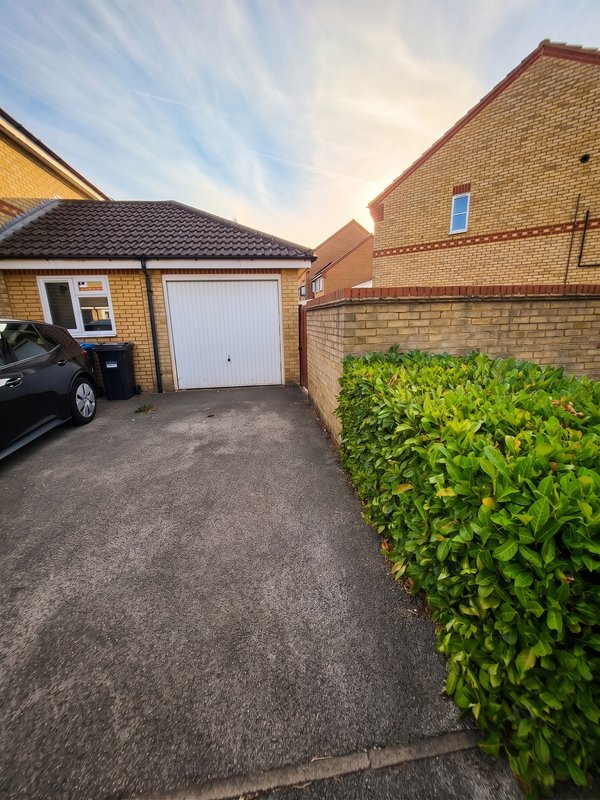 Driveway with garage, parked car, brick houses and green hedge border