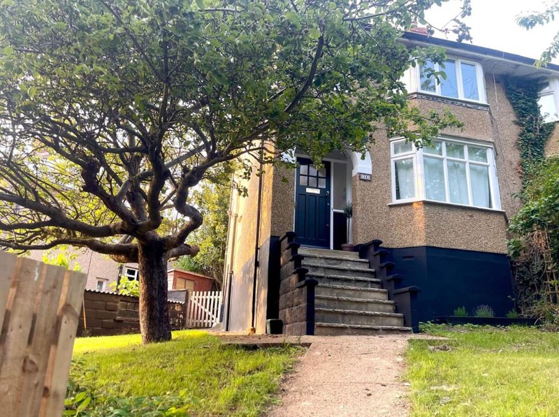 Semi-detached brick house with front garden, large tree, and driveway approach