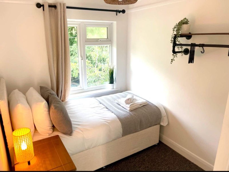 Compact bedroom with double bed, window with curtains, cushions and bedside lamp