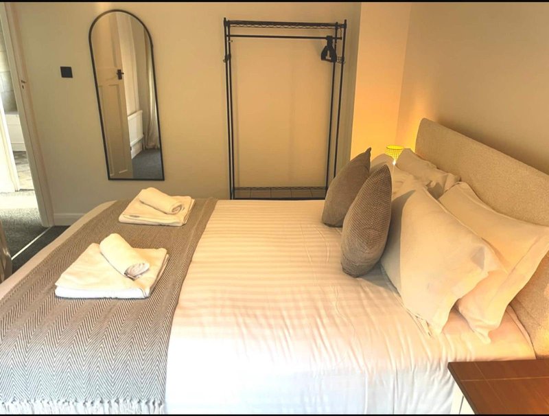 Compact bedroom with single bed, mirror, clothing rack, and neutral bedding