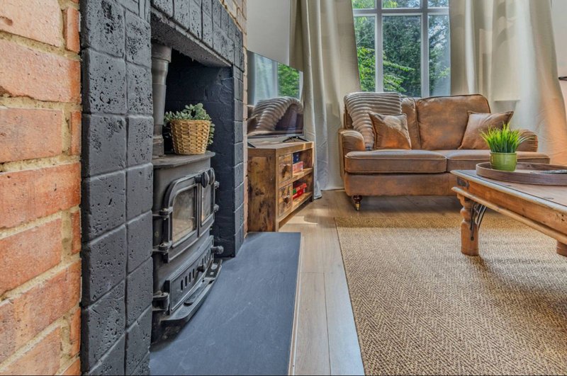 Living room with wood-burning stove, brown leather sofa, wooden table and large windows