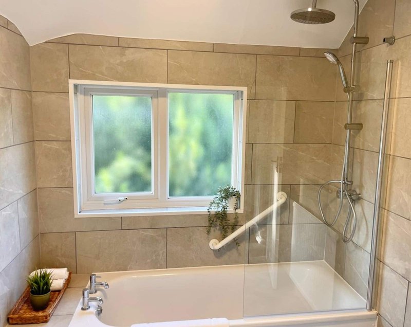 Modern bathroom with tiled walls, bathtub with glass shower screen and window