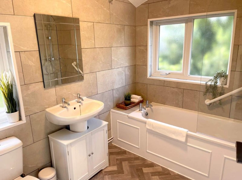Modern bathroom with pedestal sink, bathtub, window, and neutral tile walls
