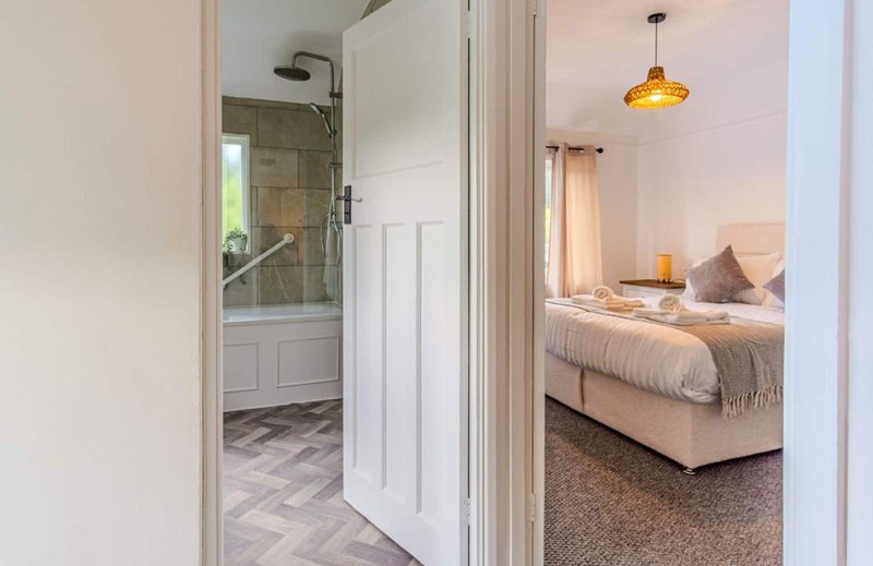 Open doorway showing ensuite bathroom and bedroom with double bed and pendant light