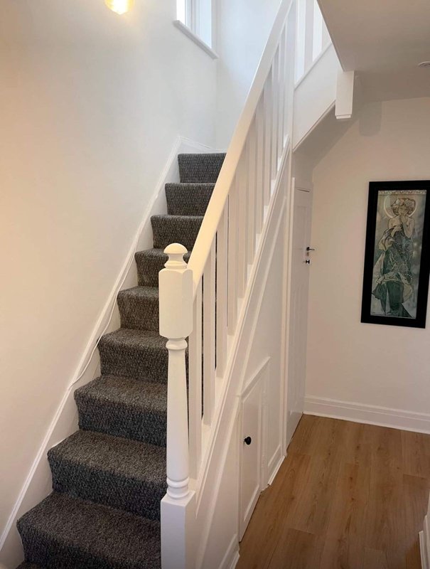 Interior staircase with gray carpet, white railings, and framed artwork on wall