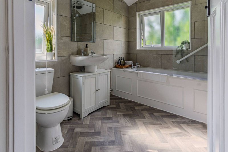 Modern bathroom with toilet, vanity sink, bathtub, herringbone floor and tiled walls