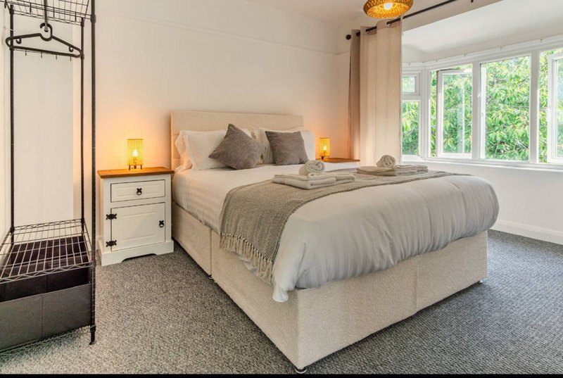 Bright bedroom with double bed, bedside tables, lamps, and en-suite shower room visible
