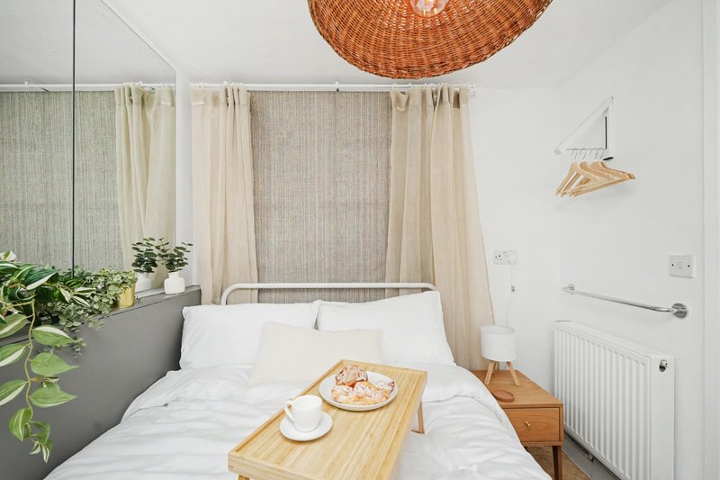 Bedroom with double bed, wooden breakfast tray, woven pendant light and neutral curtains