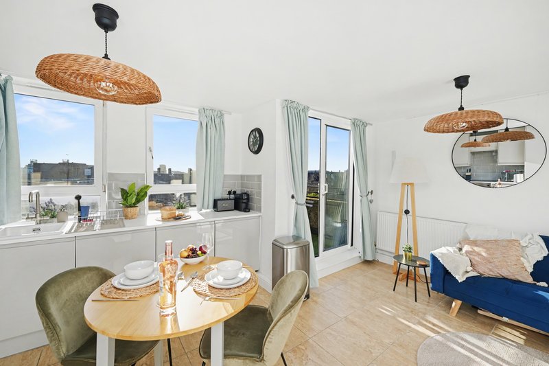 Open-plan kitchen-dining-living room with round table, blue sofa, and city views from windows
