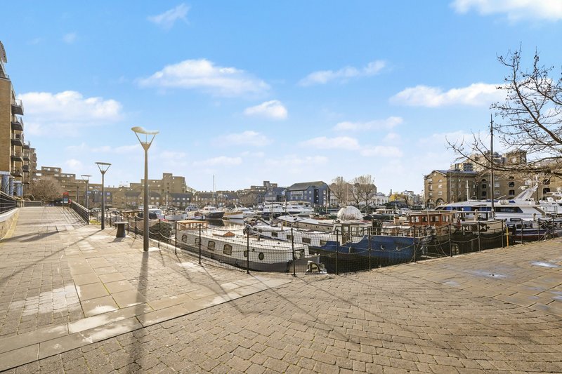 Waterfront promenade with moored narrowboats, paved walkway, street lamps and residential buildings