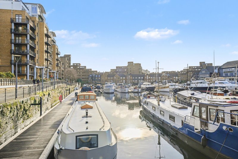 Canal-side apartment buildings with moored boats, waterfront promenade and blue sky
