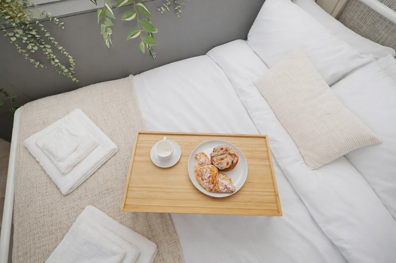 Bedroom with double bed, wooden breakfast tray with pastries and coffee, white pillows and hanging plants