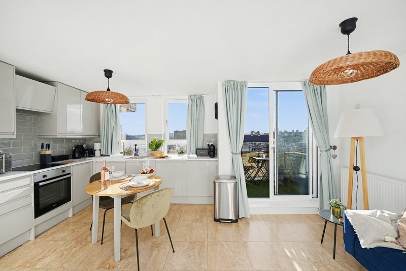 Modern kitchen and dining area with white cabinetry, wooden table, woven pendant lights and city views