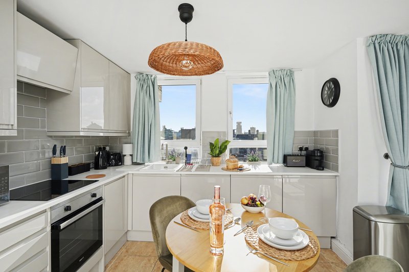 Modern kitchen with white cabinetry, dining table, woven pendant light and city views through windows