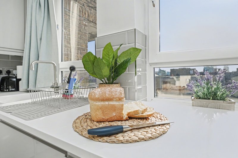 Modern kitchen with white countertop, potted plant, fresh bread and city views through windows