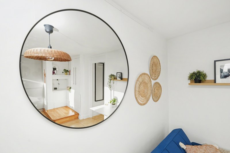 Modern bathroom with large round mirror, woven wall baskets, potted plant and blue upholstered seating