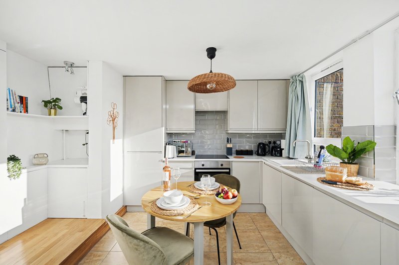 Modern white kitchen with wooden dining table, rattan pendant light and window view