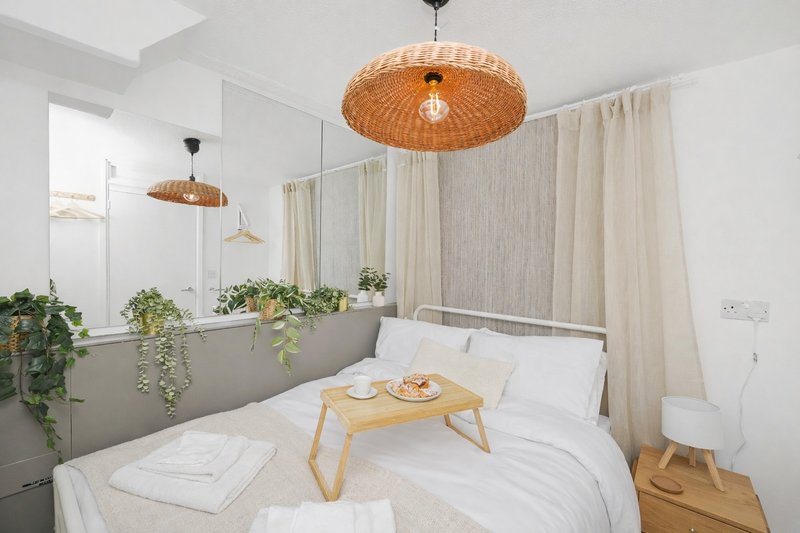 Bright modern bedroom with double bed, wooden breakfast tray, woven pendant lights and potted plants