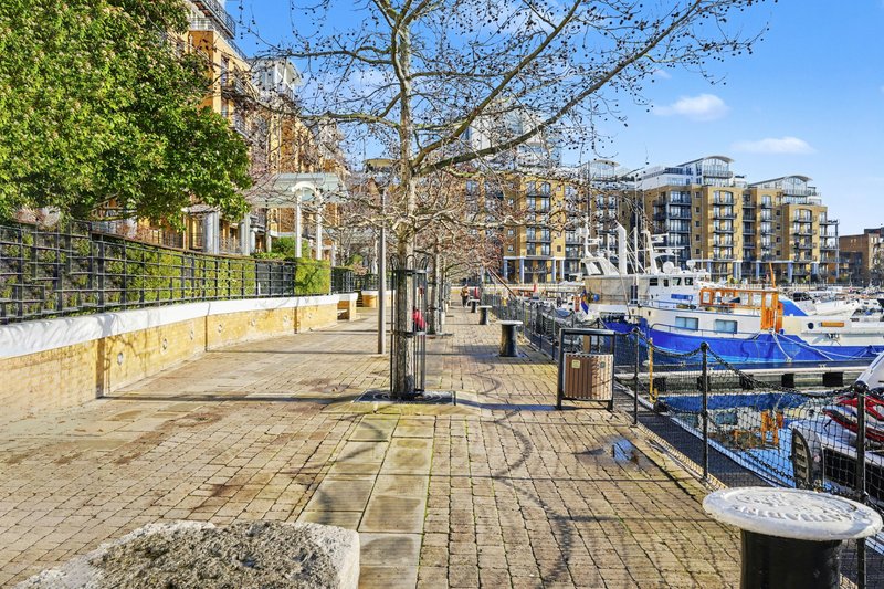 Waterfront promenade with paved walkway, trees, residential buildings and moored boats