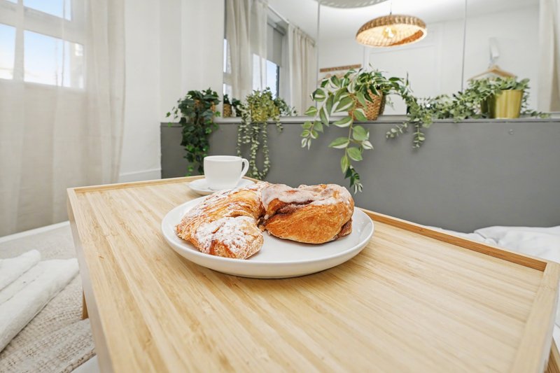Bright kitchen dining area with wooden table, pastries on white plate, potted plants and pendant light