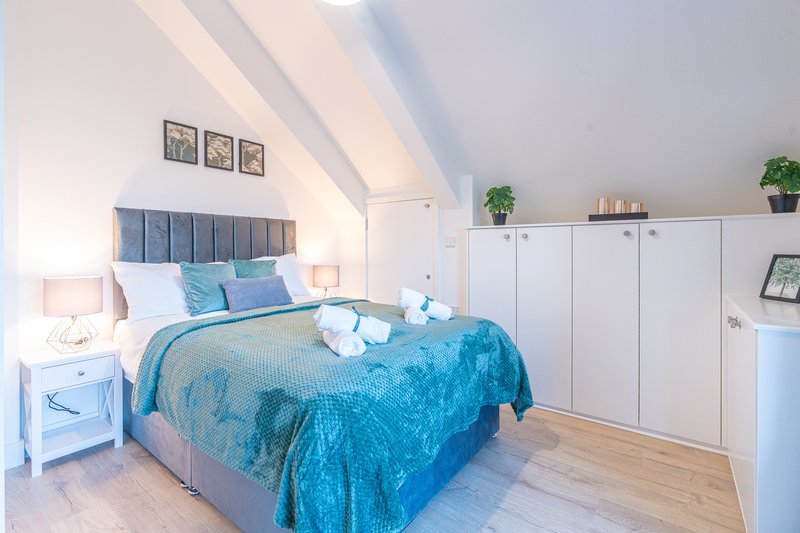 Bright attic bedroom with blue velvet bedding, white furniture, skylight windows and wooden flooring