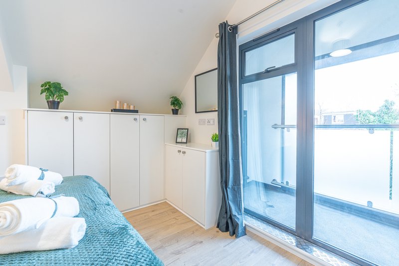 Bright bedroom with double bed, white wardrobe, wooden floor and glass door to balcony