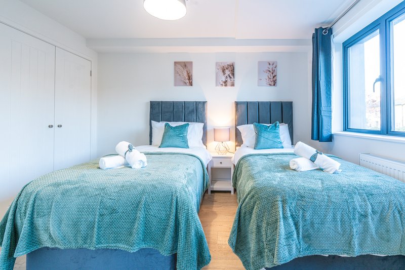 Twin bedroom with two beds, turquoise bedding, headboards, side table and blue curtains
