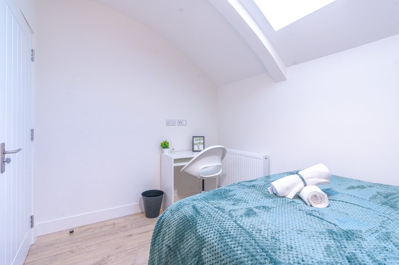 Bright modern bedroom with blue bedspread, skylight, wooden floor and desk area