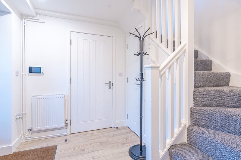 Bright hallway with wooden flooring, white doors, radiator, coat stand and carpeted staircase