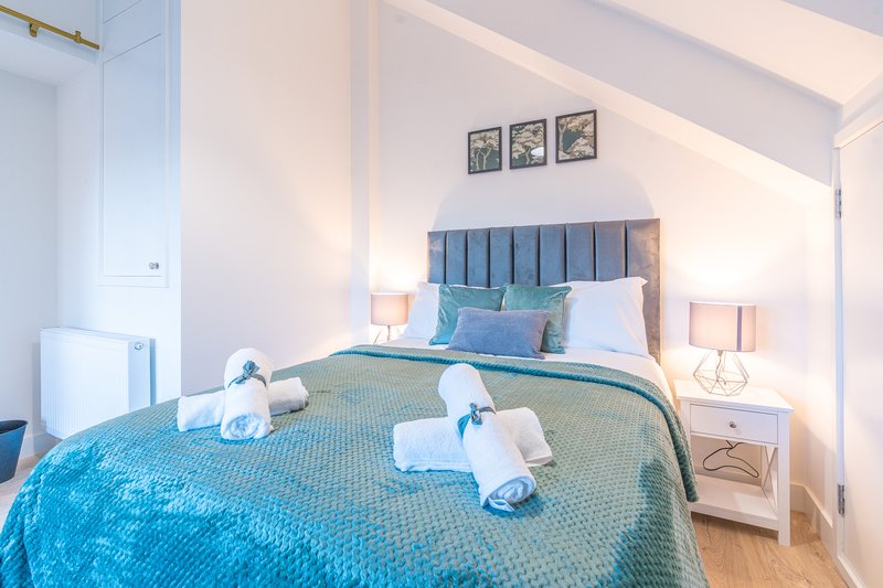 Modern bedroom with blue upholstered headboard, white bedding, rolled towels, and bedside lamps