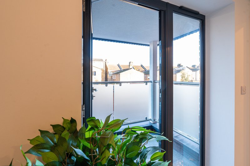 Modern room with large black-framed windows, frosted glass panel, potted green plant on windowsill, neutral walls