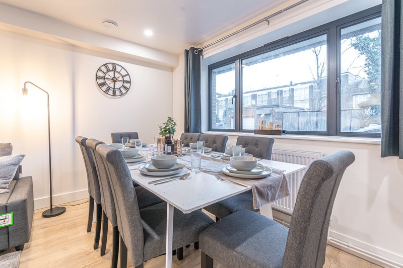 Modern dining room with white table, gray upholstered chairs, large windows and wall clock