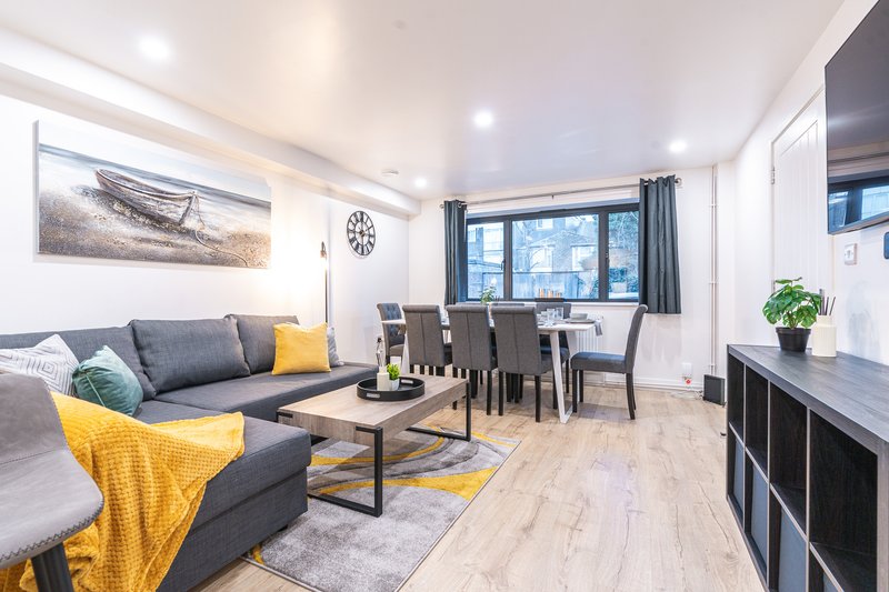 Open-plan living room with grey sofa, yellow accents, dining table and large windows